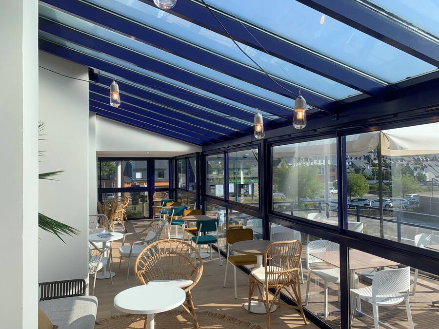 Una cafeteria moderna amb parets de vidre, mobles de vimet i lluminàries penjants.