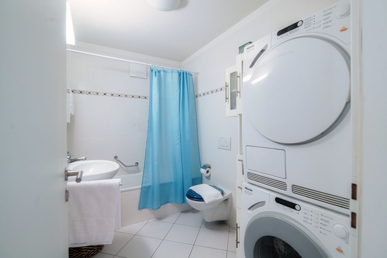 Et lille badeværelse med vaskemaskine, vask og toilet.