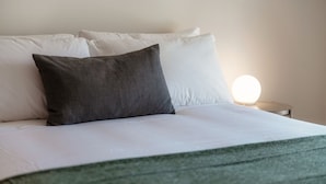 A neatly made bed with white linens and a dark gray pillow.