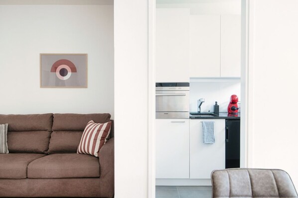 A modern living room with a brown sofa, a striped pillow, and a framed abstract artwork on the wall. - Central two-room apartment with balcony (LOCARNO CITY 2) (Locarno)