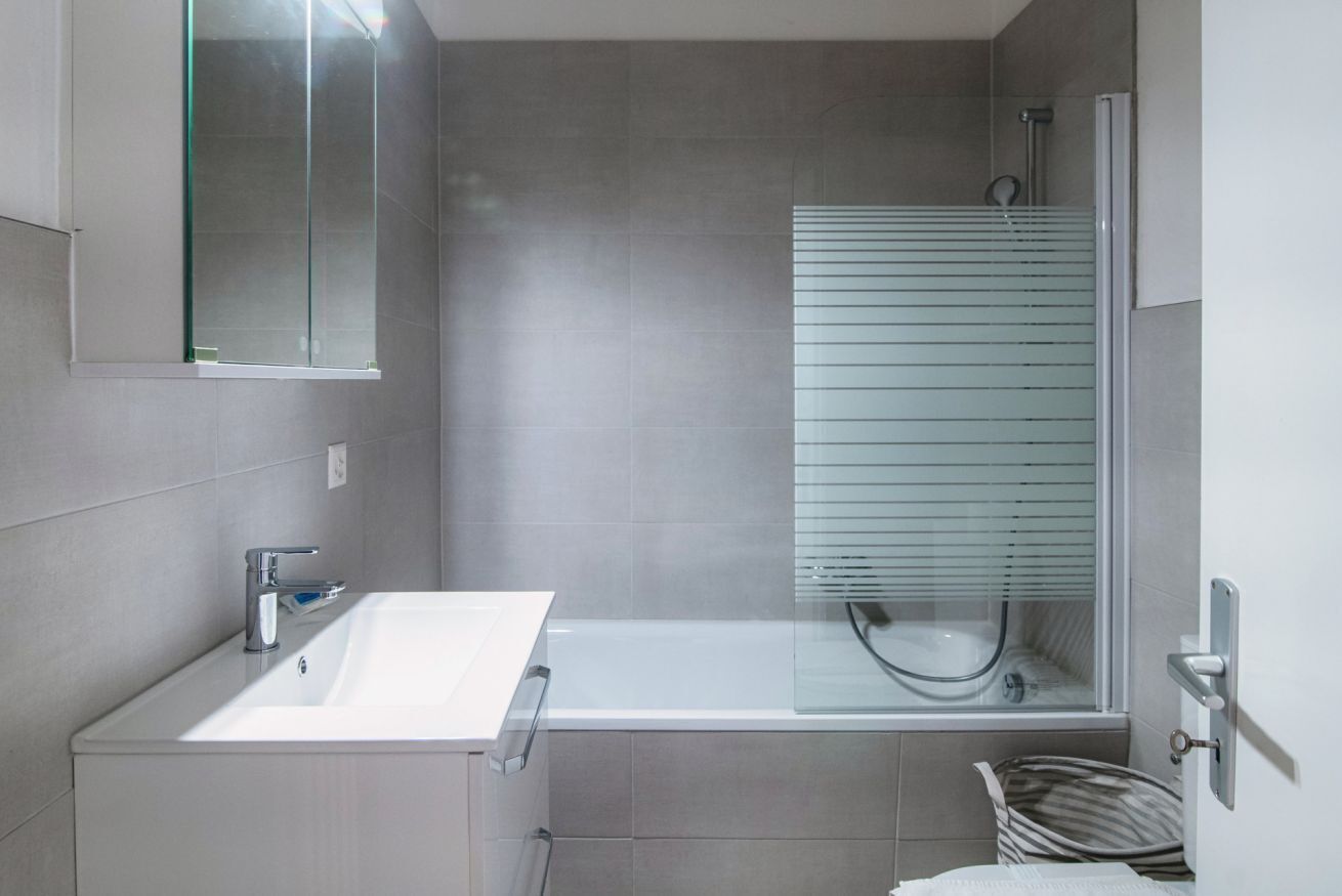 A modern bathroom with a white sink, a glass-enclosed shower, and a mirror above the sink.