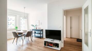A modern living room with a dining area, a flat-screen TV on a white stand, and a blue sideboard.