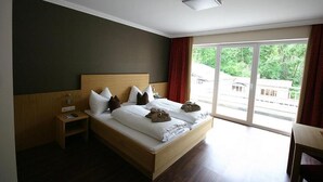 A hotel room with a large bed, a nightstand, and a view of greenery through the window.