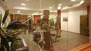 A gym with exercise equipment, a mirror wall, and wooden flooring.