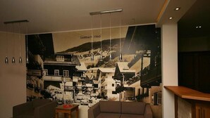 A lobby with a large mural of a town, a sofa, two small tables, and hanging lights.