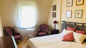 Une pièce avec deux lits, une petite table ronde, deux fauteuils, une lampe et des tableaux encadrés accrochés au mur.