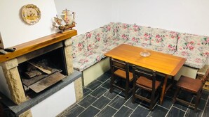 Une pièce d’angle avec une cheminée en pierre, un canapé à motifs floraux, une table en bois et des chaises assorties.