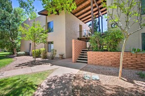 Un bâtiment moderne avec un escalier en briques menant à un balcon, entouré d’arbres et d’une pelouse bien entretenue.