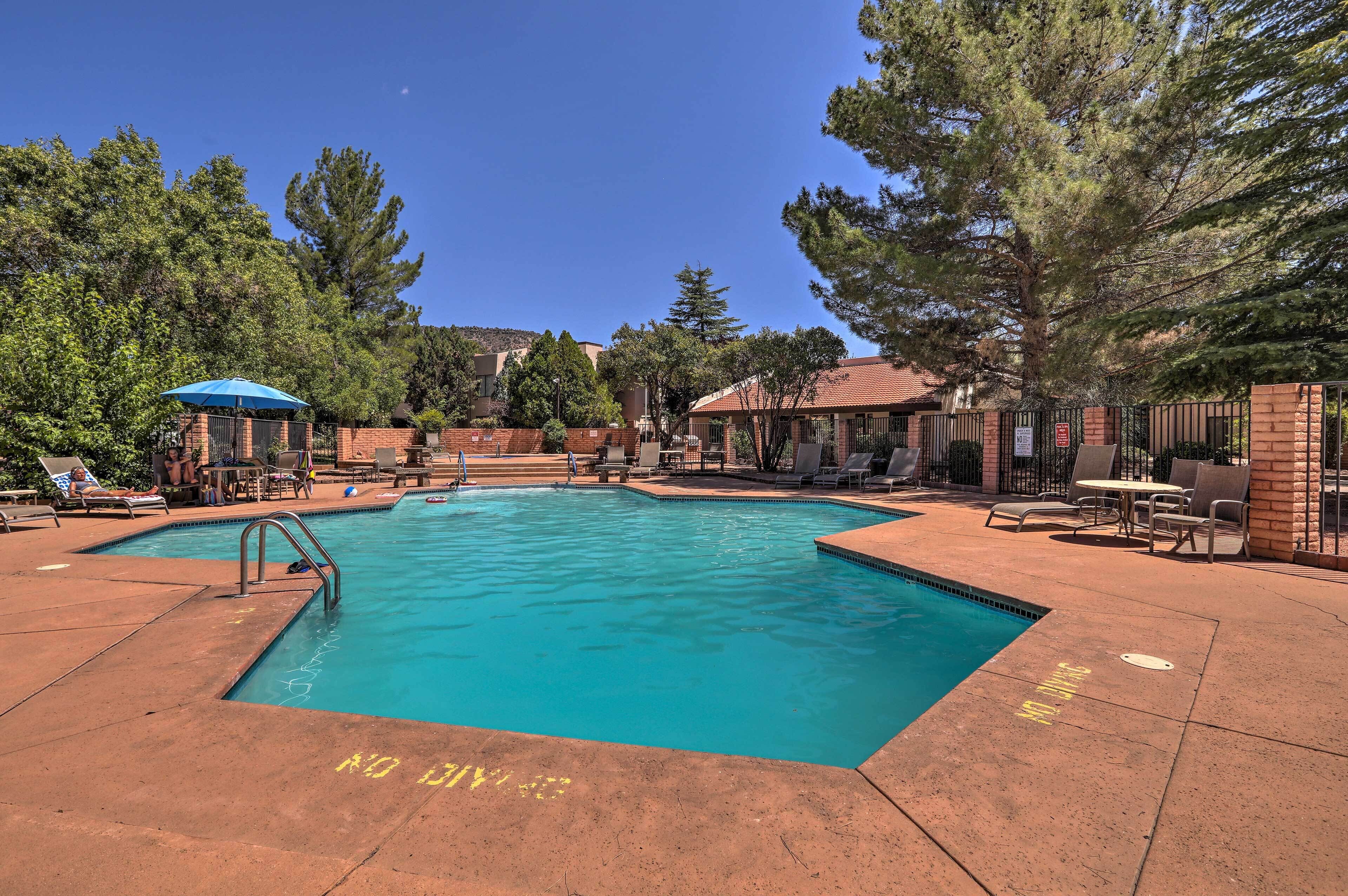 A swimming pool with lounge chairs and umbrellas, surrounded by trees and buildings.