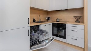 Une cuisine moderne avec des meubles blancs, un lave-vaisselle, un four et une machine à café.