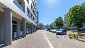 Un bâtiment moderne avec une allée pavée, des voitures garées et un banc.