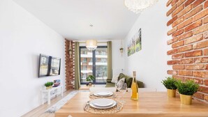 Un coin repas avec une table en bois dressée pour deux personnes, un mur en briques et une vue sur un balcon extérieur, visible à travers une porte vitrée.