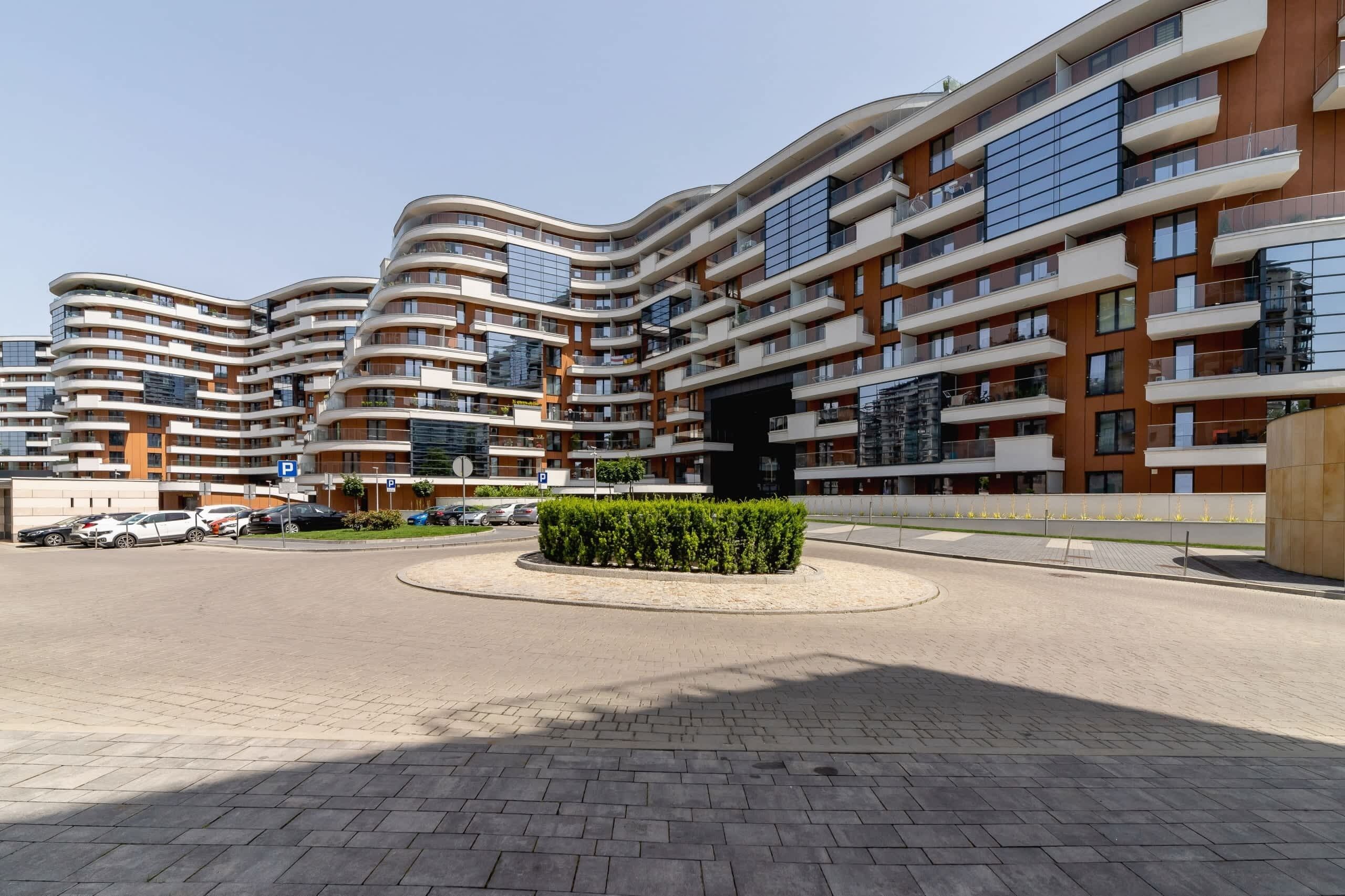 A modern apartment complex with multiple balconies, a central landscaped area, and a parking lot.