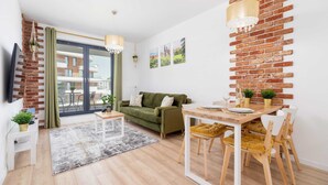 Un salon moderne avec un canapé vert, une table à manger en bois et un mur en briques qui sert d’élément décoratif.
