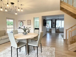 A spacious living area with a round wooden dining table, two white cushioned chairs, a modern chandelier, and a staircase leading to an upper level. - Impeccable 2-bed House in Albești (Albesti)