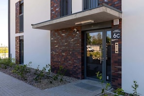 Un bâtiment moderne avec une façade en briques, une entrée en verre et une enseigne indiquant l’adresse « 6C ».