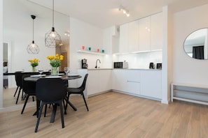 Une cuisine moderne avec des meubles blancs, un coin repas doté d’une table ronde et de chaises, et des luminaires suspendus au-dessus de la table.