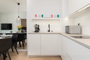 Une cuisine moderne avec des meubles blancs, un plan de travail, une machine à café, un four à micro-ondes et un évier.