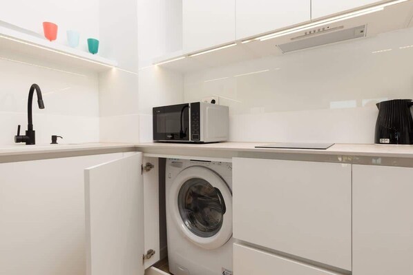 A compact kitchen with a washing machine, a microwave, and a sink.