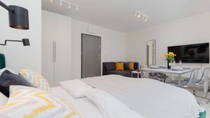 A modern hotel room with a large bed, a desk with a chair, a flat-screen TV, and a door.