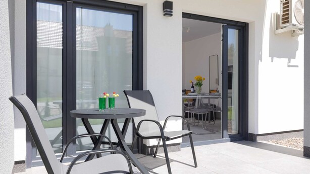An outdoor patio with a round table and chairs, a sliding glass door leading to an indoor area, and a small air conditioning unit mounted on the wall.