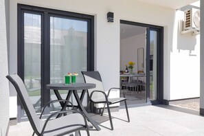An outdoor patio with a round table and chairs, a sliding glass door leading to an indoor area, and a small air conditioning unit mounted on the wall.