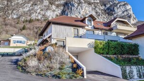 A modern house with a sloped roof, a staircase leading to the entrance, and a view of a mountainous landscape. - Apartment with 180° Lake & Mountain Views (Veyrier-du-Lac)