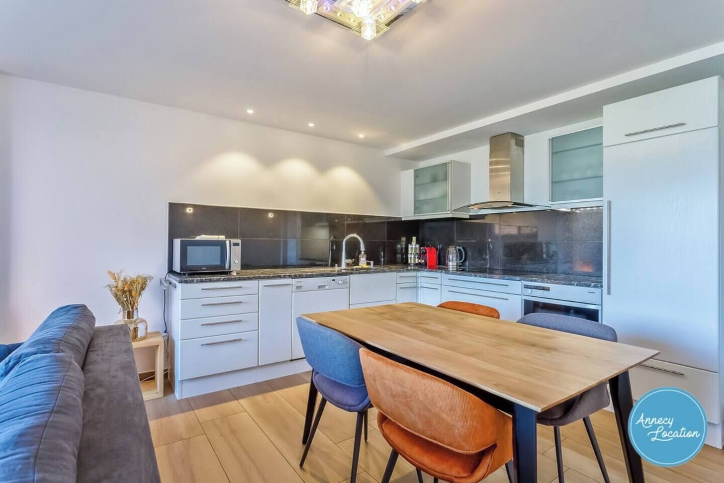 Une cuisine moderne avec des meubles blancs, une table à manger en bois et deux chaises.