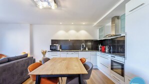 A modern kitchen with a wooden dining table, grey chairs, and a grey sofa. - Apartment with 180° Lake & Mountain Views (Veyrier-du-Lac)