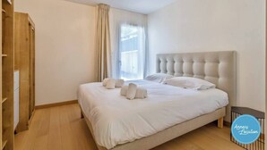 A bedroom with a large bed, a wooden wardrobe, and a window with curtains. - Apartment with 180° Lake & Mountain Views (Veyrier-du-Lac)