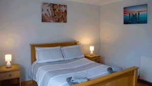 A bedroom with a wooden bed, white bedding, two bedside lamps, and artwork on the walls. - 3 Bed Bungalow - Sleeps 6 - Pet Friendly - Parking (Stranraer)