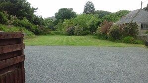 A gravel driveway leading to a grassy area with a wooden fence on the left and a house with a sloped roof on the right. - 3 Bed Bungalow - Sleeps 6 - Pet Friendly - Parking (Stranraer)