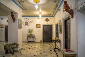 Un couloir doté d’un sol à motifs, d’une statue en bois, d’une porte ornée d’un cadre décoratif et d’un luminaire fixé au mur.