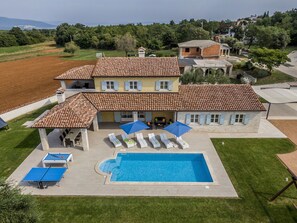 Une grande maison avec une piscine, un espace salon extérieur et un court de tennis.