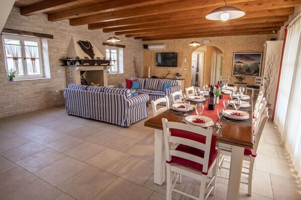 Un grand salon comprenant un canapé, une table à manger dressée pour le repas et une cheminée.