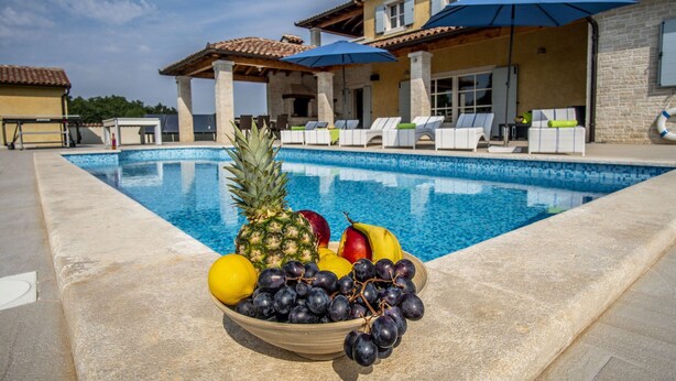 Ein Poolbereich mit Obstschale, Liegestühlen und Sonnenschirmen.