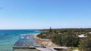 A coastal road with a clear view of the ocean, a rocky shoreline, and a forested area. - Tula - waterfront reserve (Currarong)