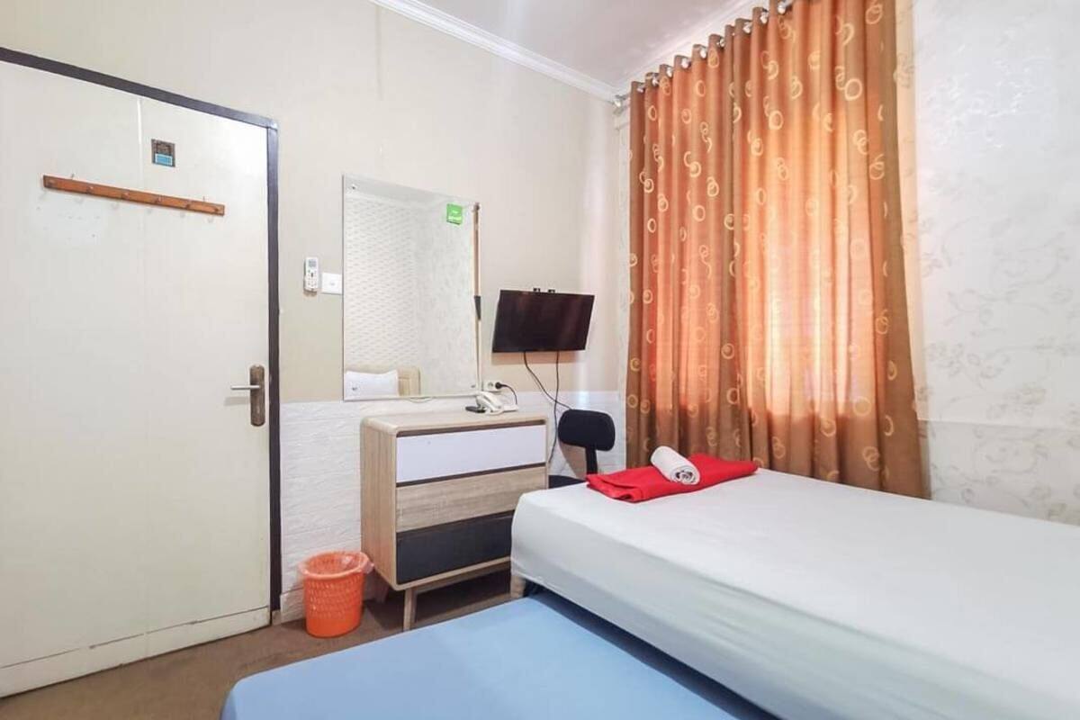A hotel room with a bed, a desk with a chair, a television, and a window with curtains.