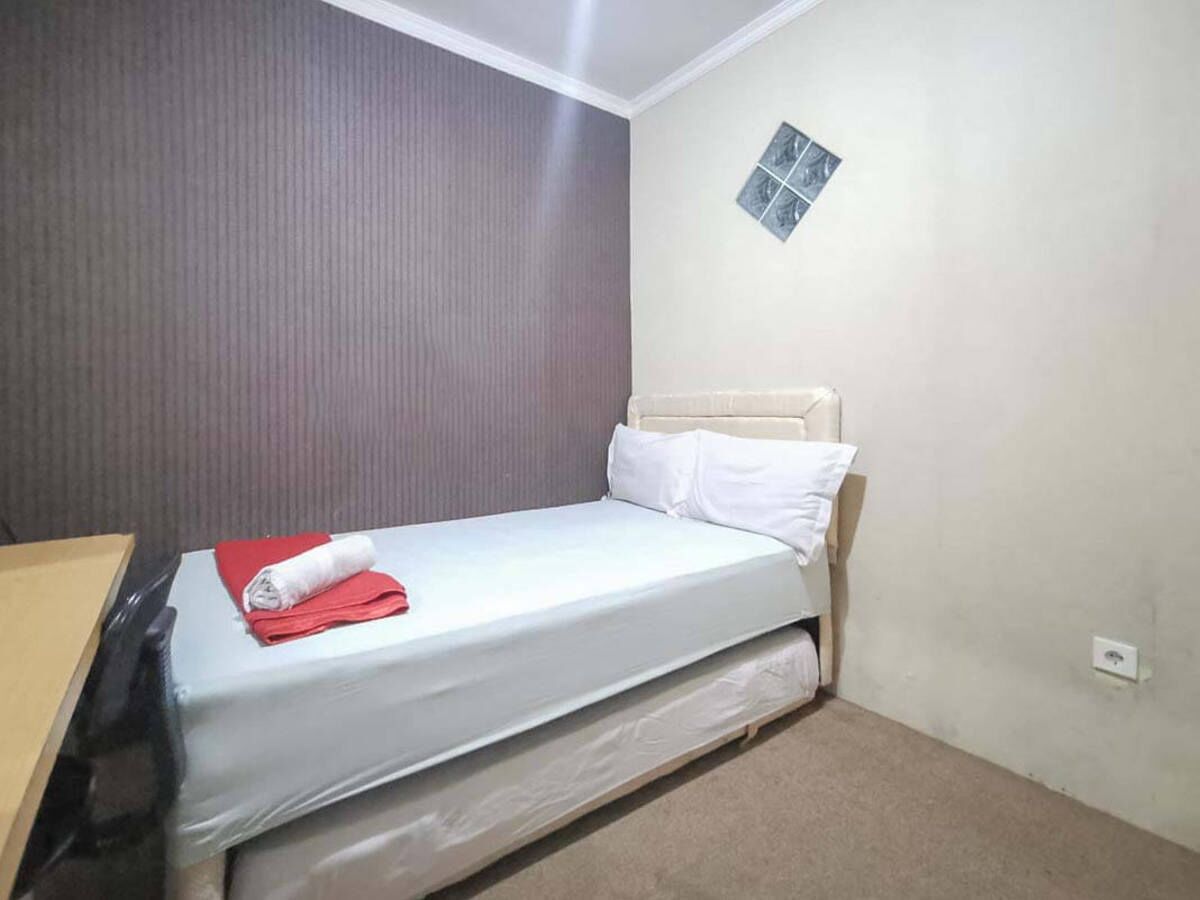 Una cama individual con colchón y almohadas blancos, una toalla roja y un cabecero.