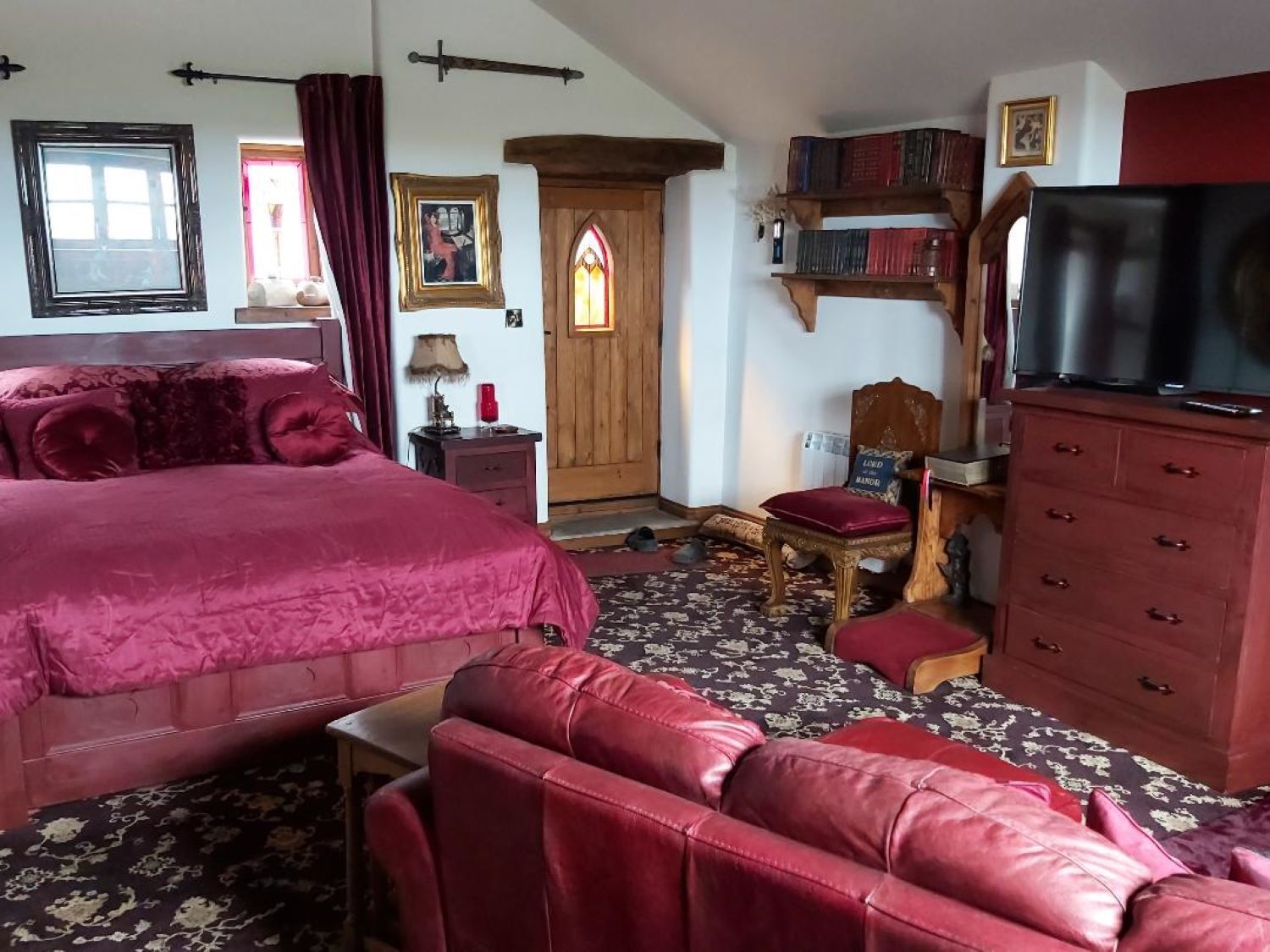A bedroom with a large bed, a wooden wardrobe, a television, and a bookshelf.