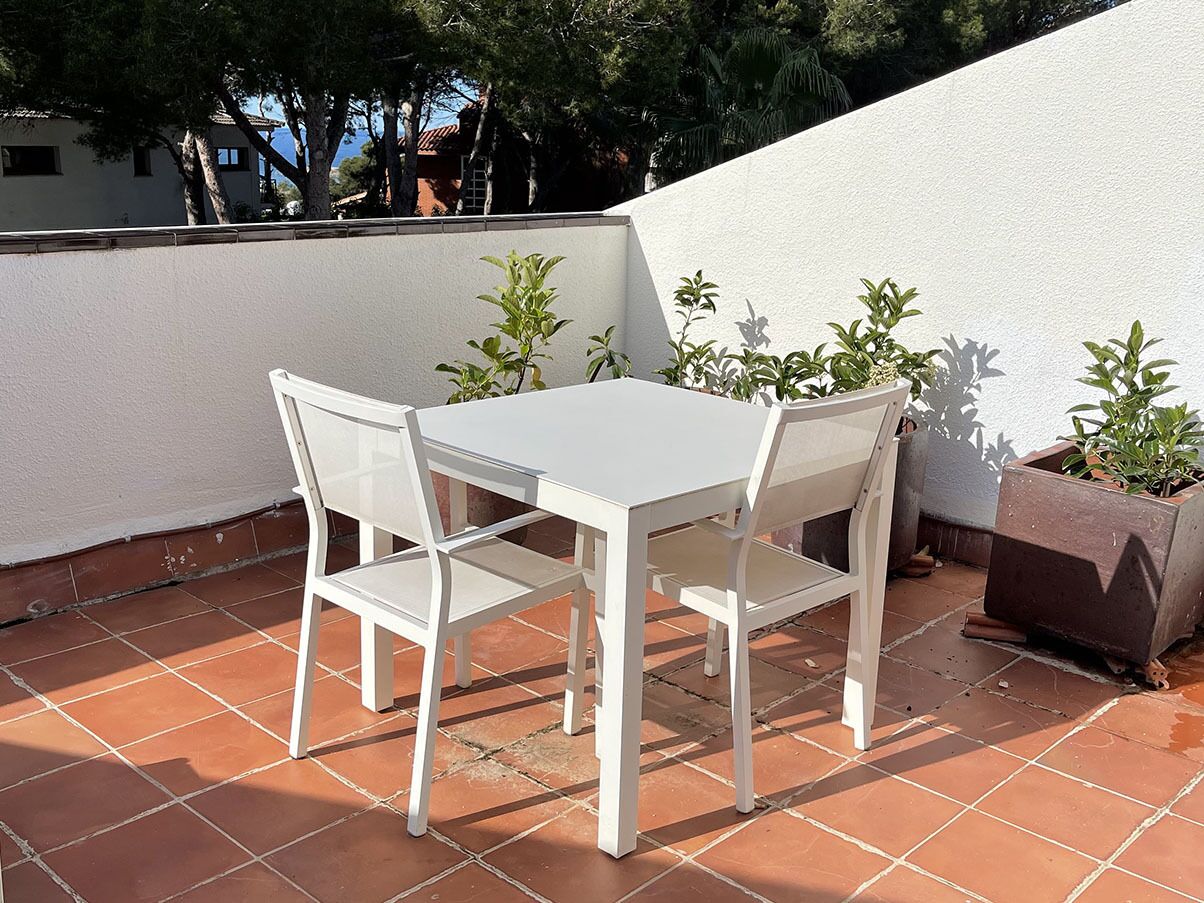 A white table and chairs on a tiled patio with potted plants.