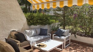 Ein Sitzbereich im Freien mit einem gelb-weiß gestreiften Sonnenschirm, gepolsterten Sofas und einem kleinen Tisch.