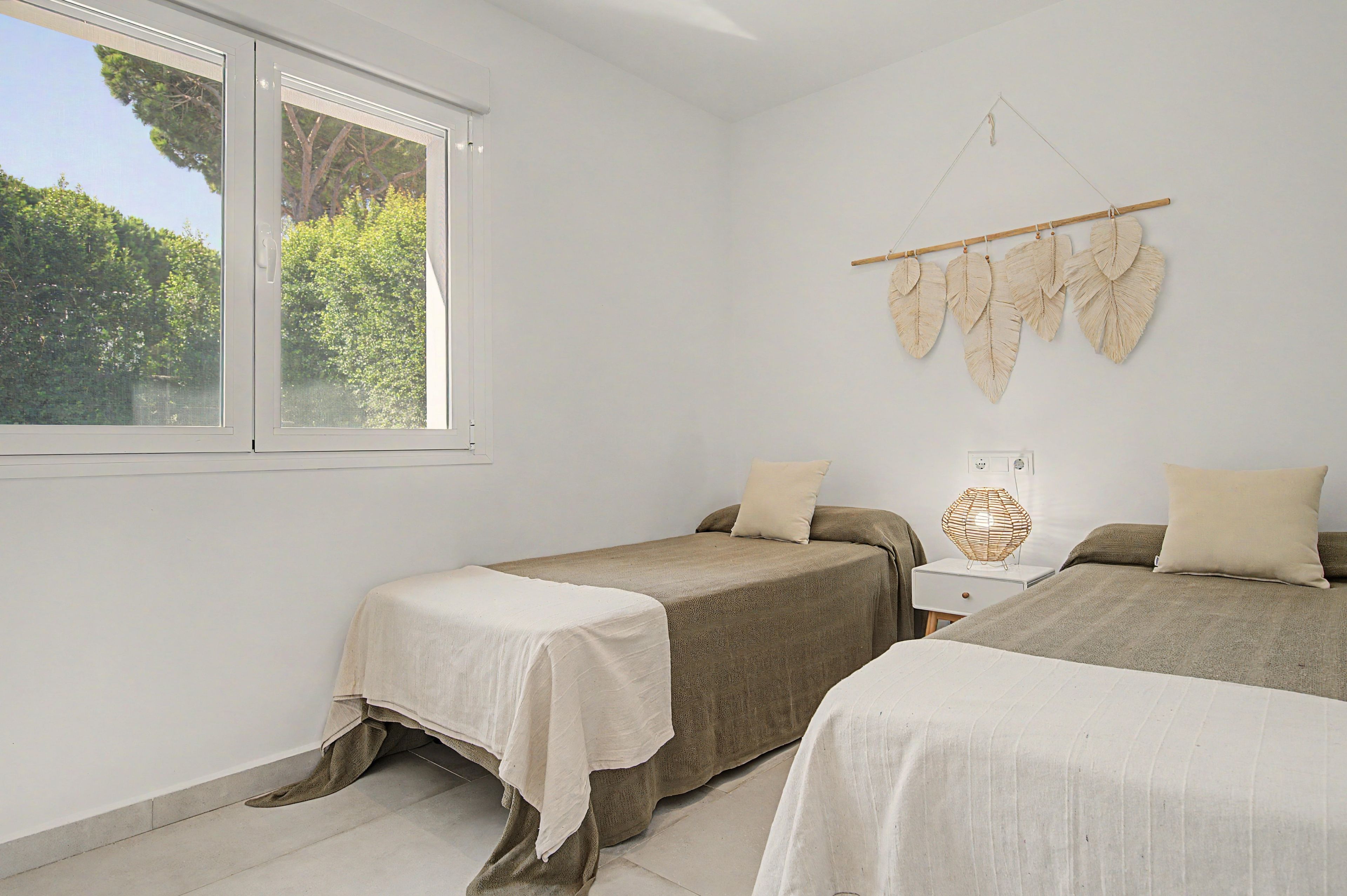Une chambre avec deux lits, une fenêtre donnant sur la forêt et un élément décoratif fixé au mur.