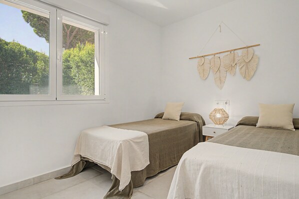 A bedroom with two beds, a window with a view of trees, and a wall-mounted decoration.