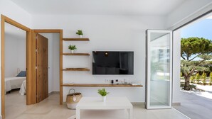 A modern living room with a TV, wooden shelves, a white table, and a view of the outdoors. - Casa Robert in Conil with Pool, Hot Tub, Garden, and Wi-Fi (Conil)
