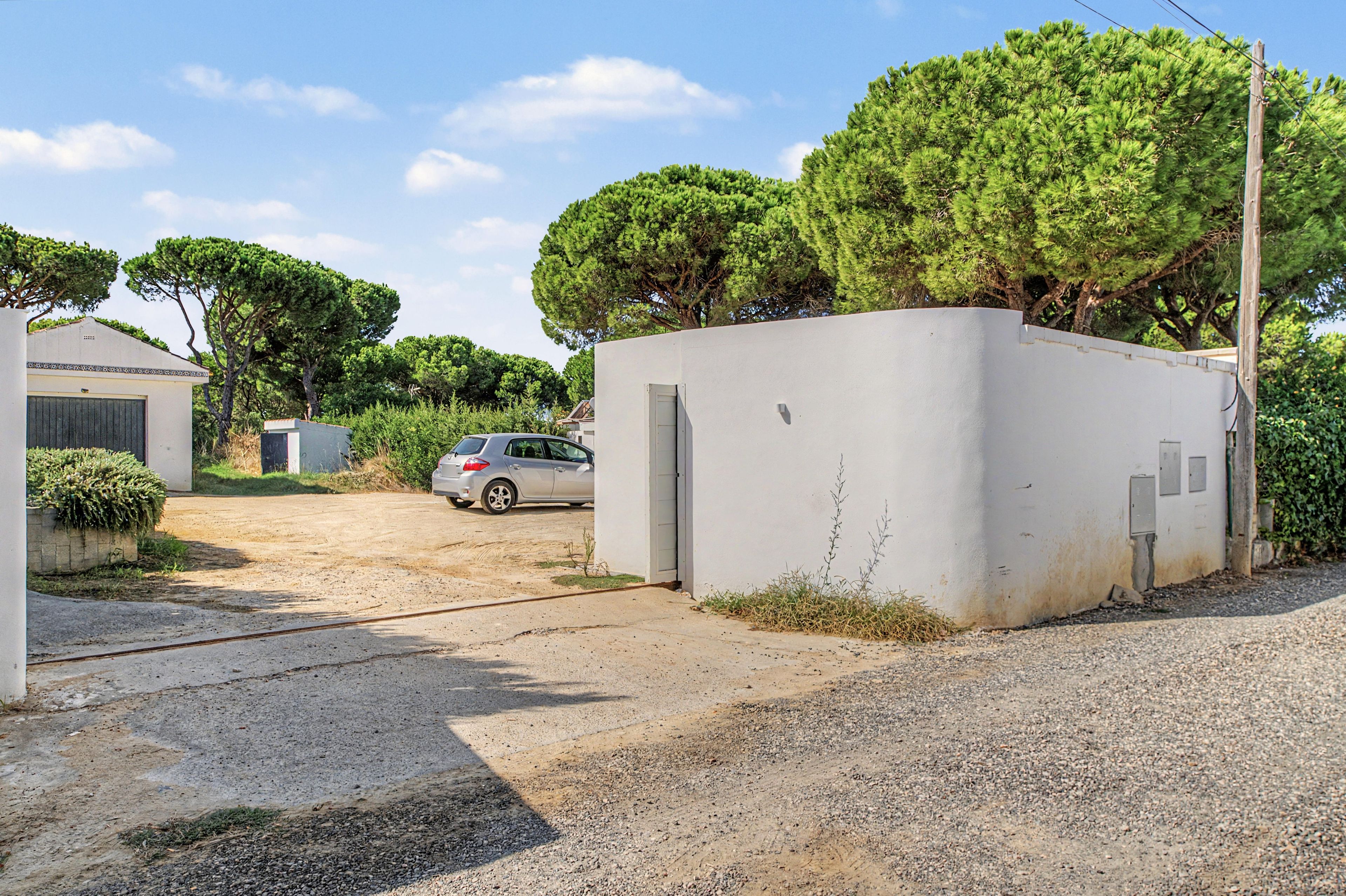 Zona residencial com entrada pavimentada, um carro estacionado e um prédio branco com garagem.