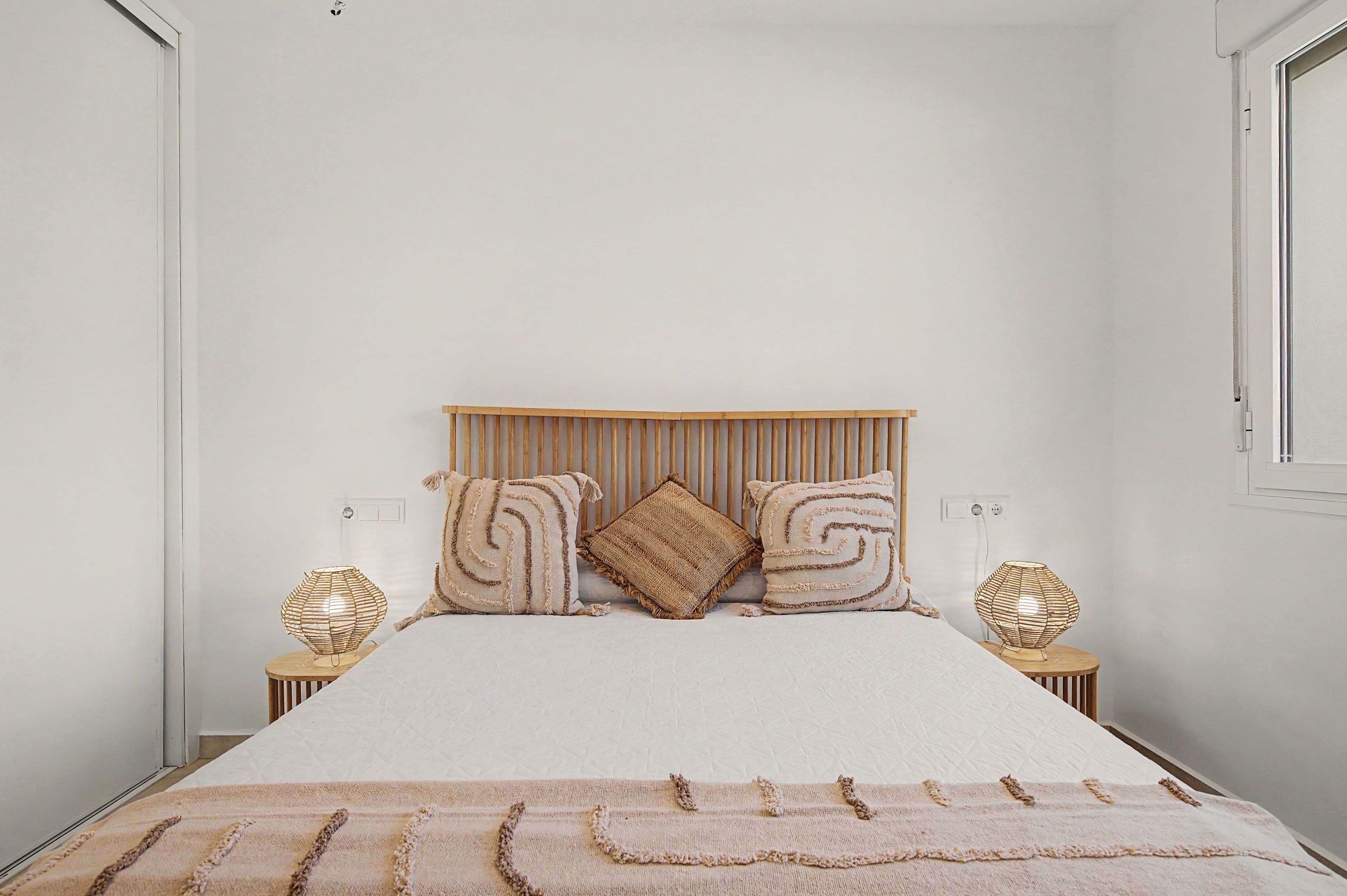 Un letto con una testiera in legno, due lampade sui comodini e una coperta decorata.