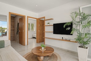 A modern living room with a wooden floor, a round coffee table, a flat-screen TV mounted on the wall, and a large potted plant.