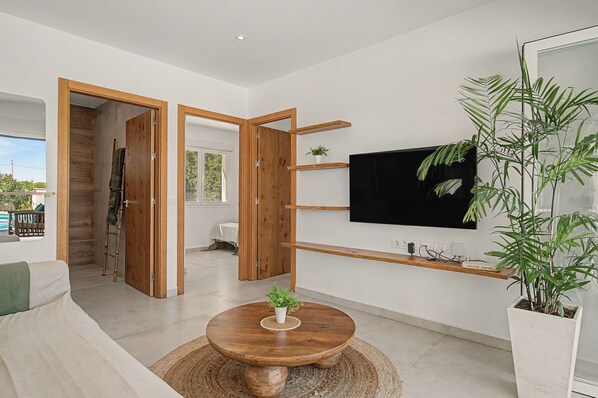 Un salon moderne avec un plancher en bois, une table basse ronde, un téléviseur à écran plat fixé au mur et une grande plante en pot.