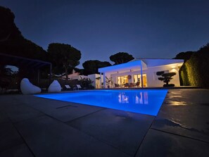 A modern house with a swimming pool, outdoor seating, and a well-lit patio area.